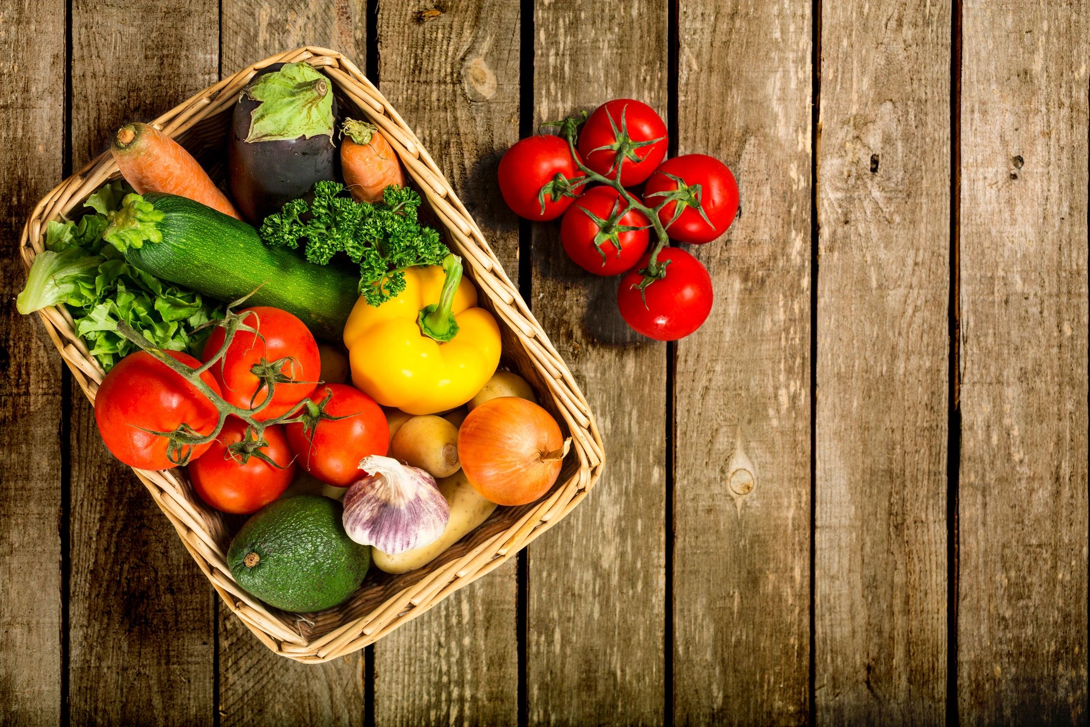 Top-down view of fresh vegetables in a basket on a wooden table